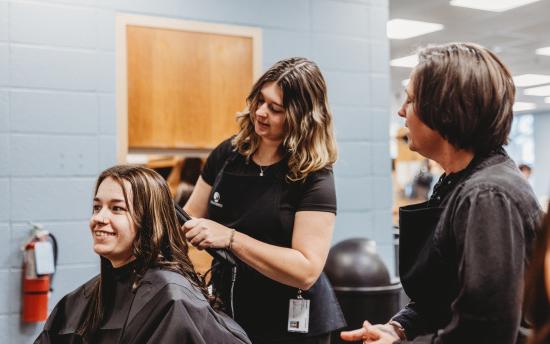 A cosmetology student is giving a haircut while the instructor supervises